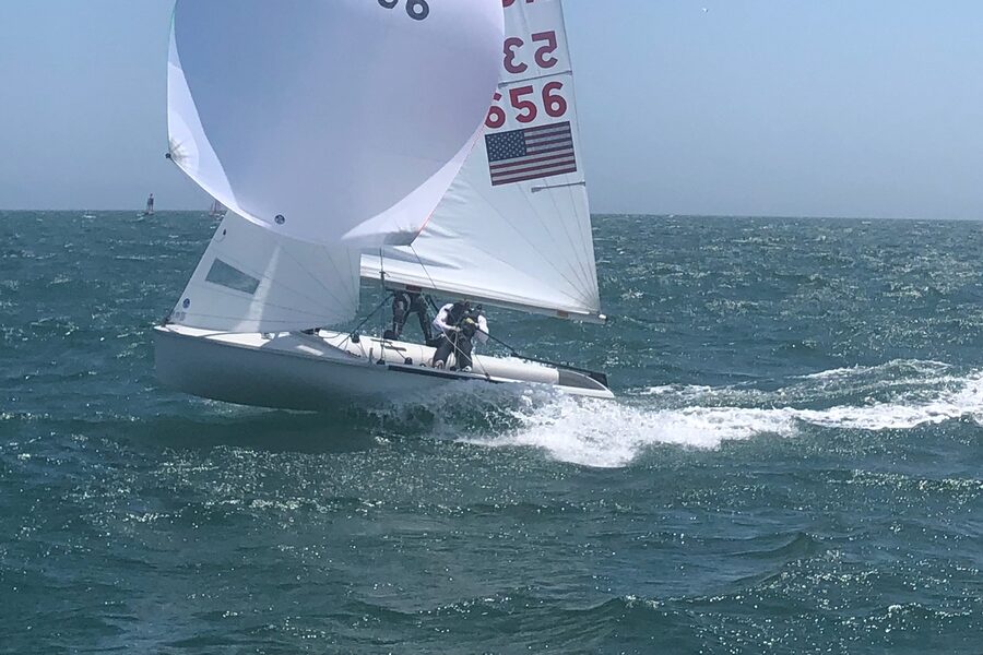 An International 420 dinghy planing under spinnaker, hull visible