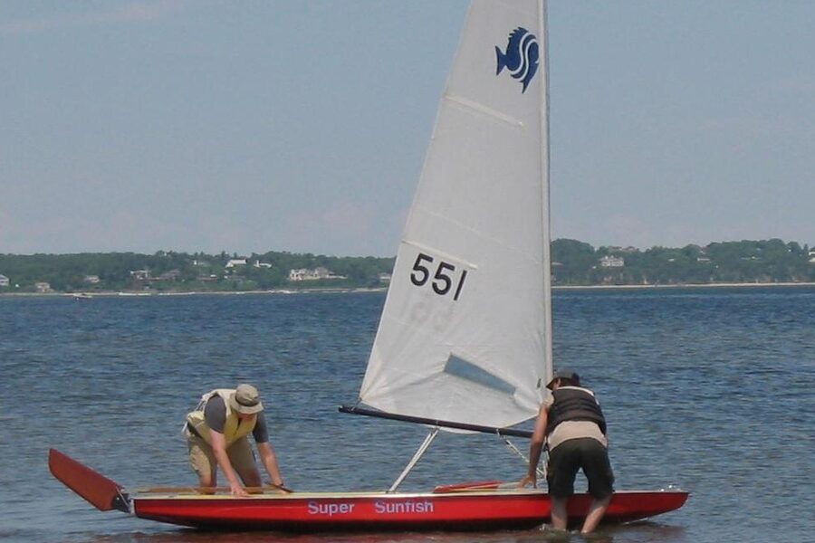 A Sunfish sailboat launching into the water, hull visible